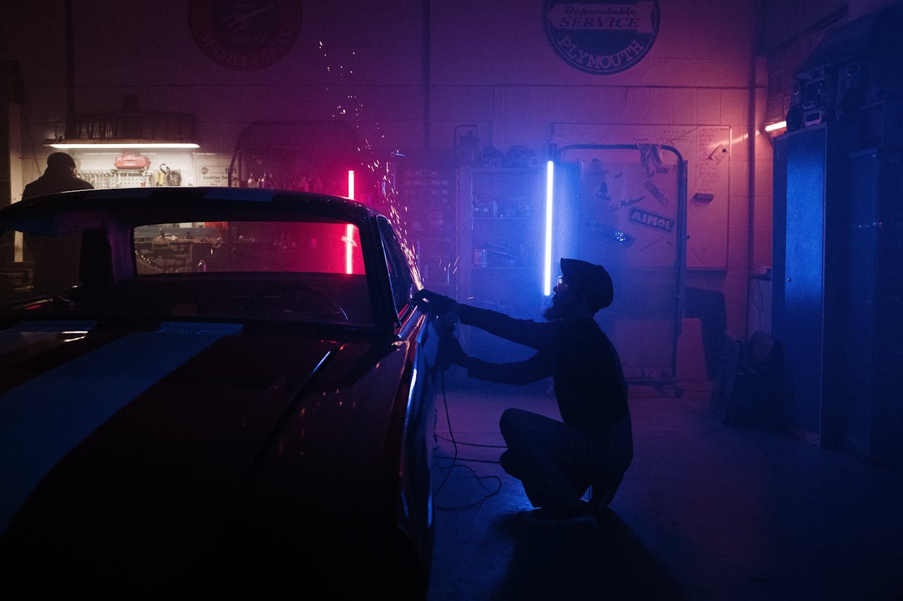 Services A mechanic works on a car in a neon-lit garage, creating a vibrant, moody atmosphere.