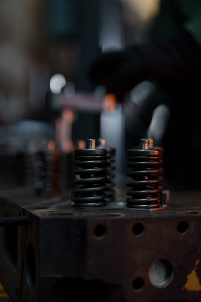 Services A detailed view of engine valve springs in a dimly lit repair shop, highlighting mechanical intricacies.