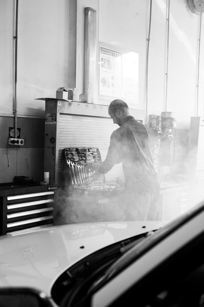 About Mechanic in a garage performing vehicle maintenance amidst tools and equipment in a smokey atmosphere.